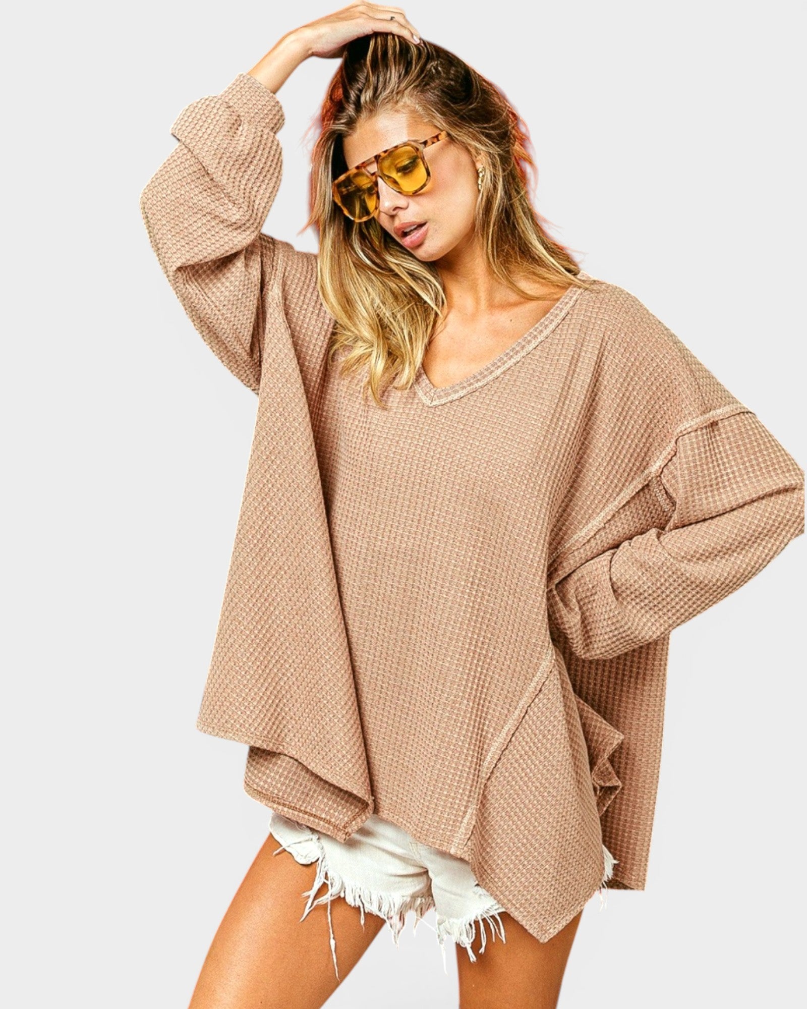 Woman wearing a beige oversized sweater and sunglasses on a white background