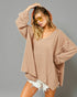 Woman wearing a beige oversized sweater and white shorts against a gray background