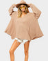 Woman wearing a beige oversized sweater and hat with sunglasses on a plain background