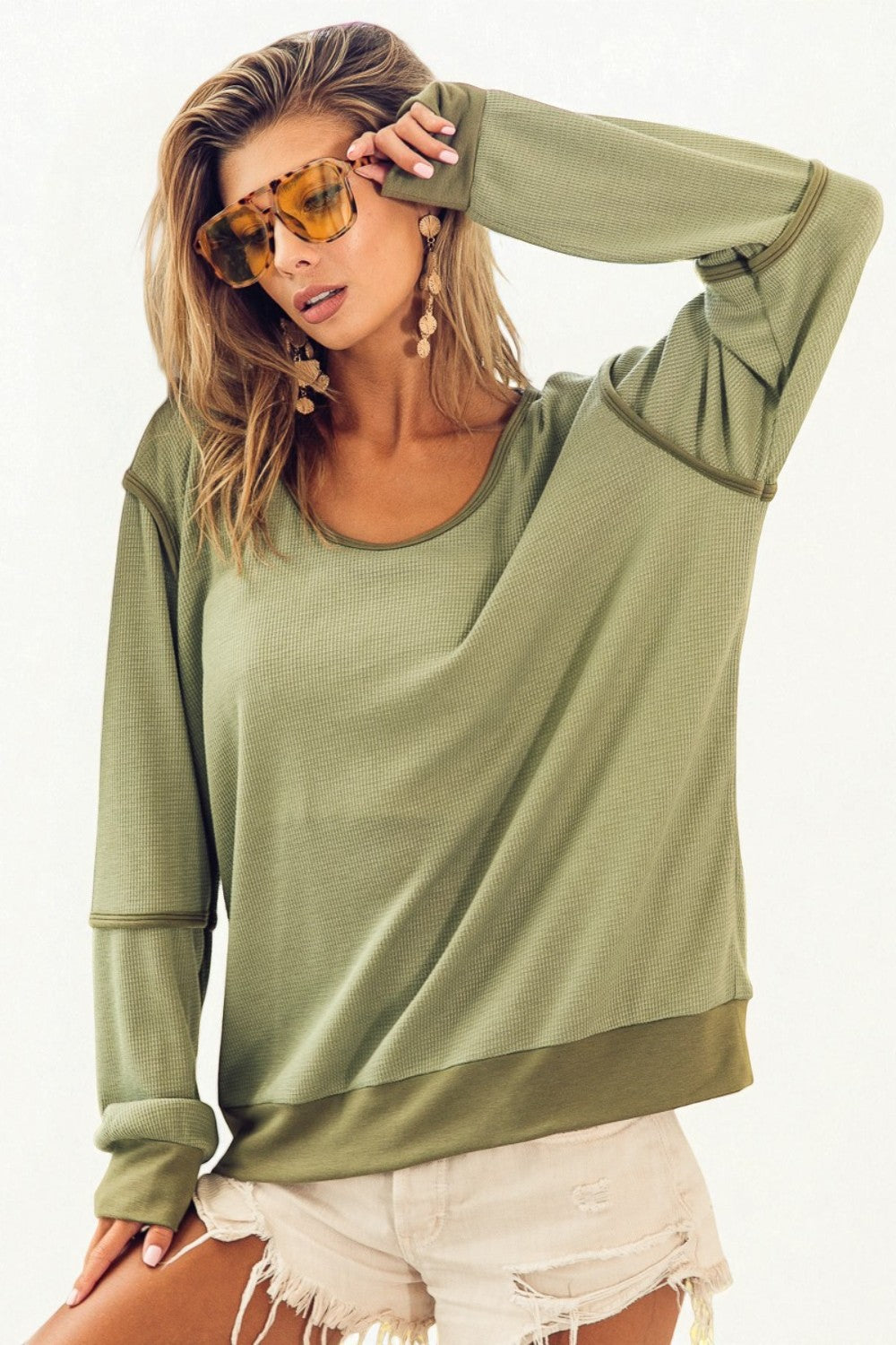 Woman wearing an olive green oversized sweatshirt and white shorts on a white background