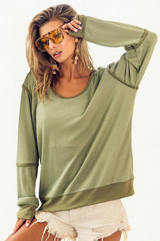 Woman wearing an olive green oversized sweatshirt and white shorts on a white background