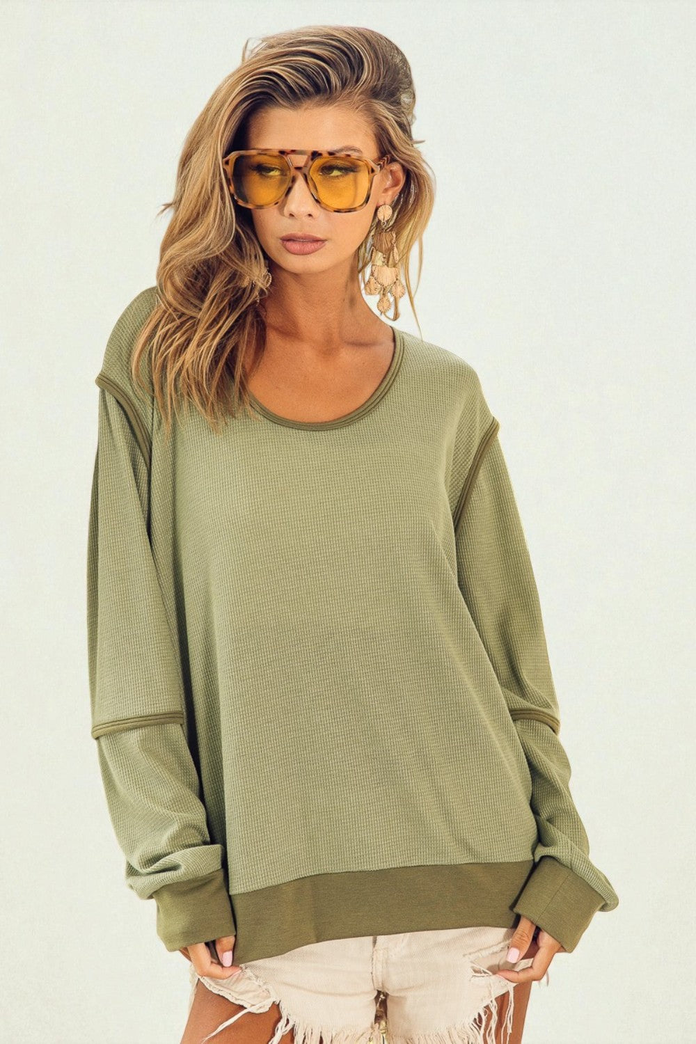 Woman wearing an olive green sweatshirt and sunglasses on a white background