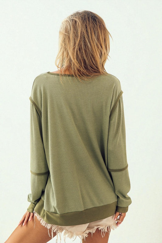 Person wearing an olive green long-sleeve top with a plain background