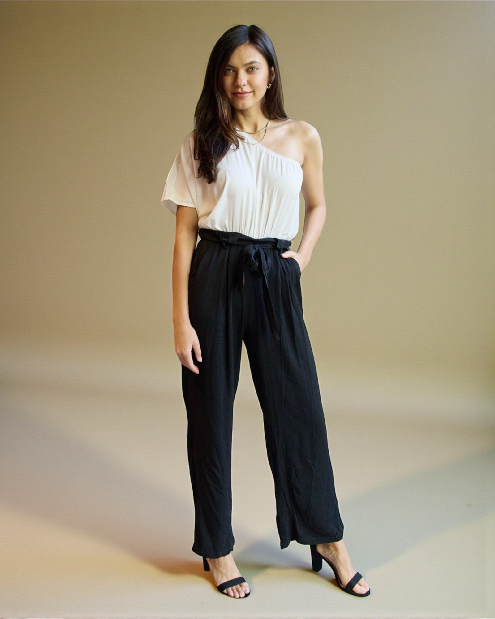 Woman wearing a white top and black pants against a beige background