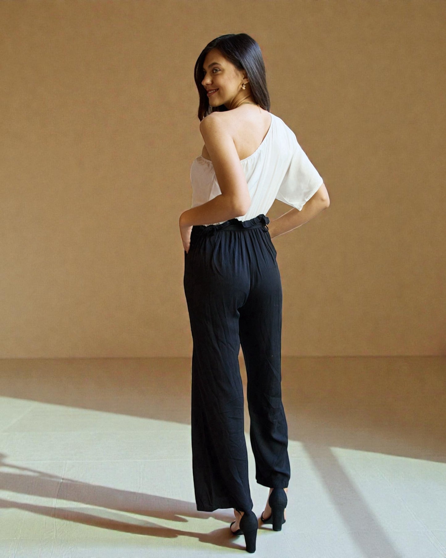 Woman wearing a white top and black pants against a beige background