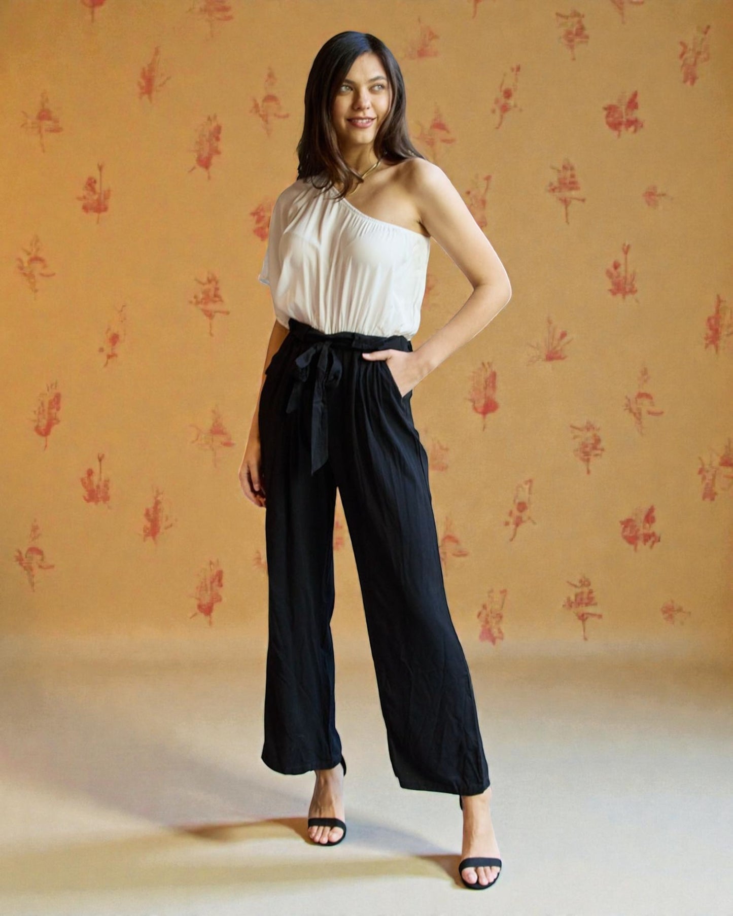 Woman wearing a white top and black pants against a patterned beige background