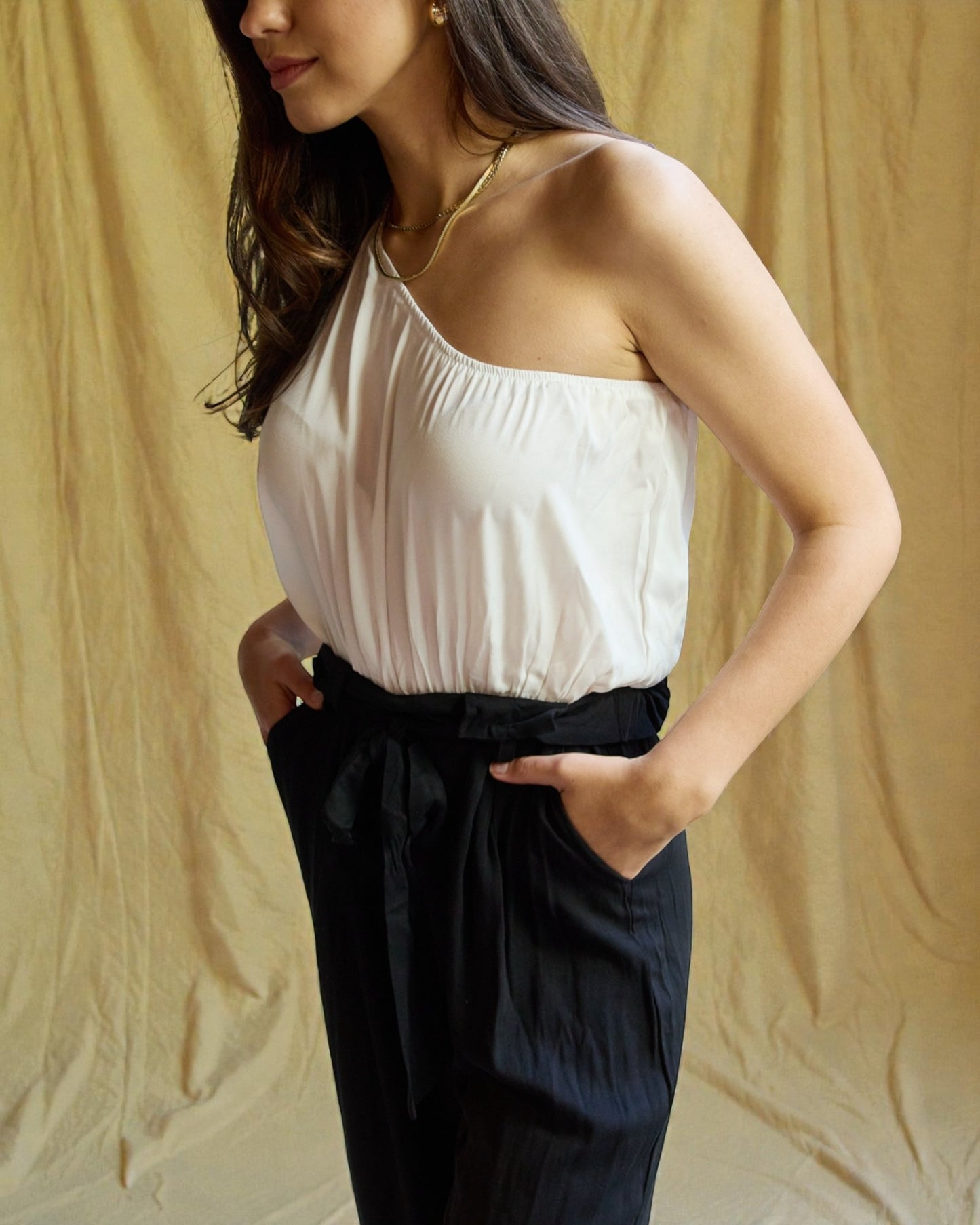 Woman wearing a white top and black pants against a beige background