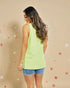 Woman wearing a light green sleeveless top and denim shorts on a beige background with star patterns.