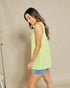 Woman wearing a light green sleeveless top and denim shorts against a beige background