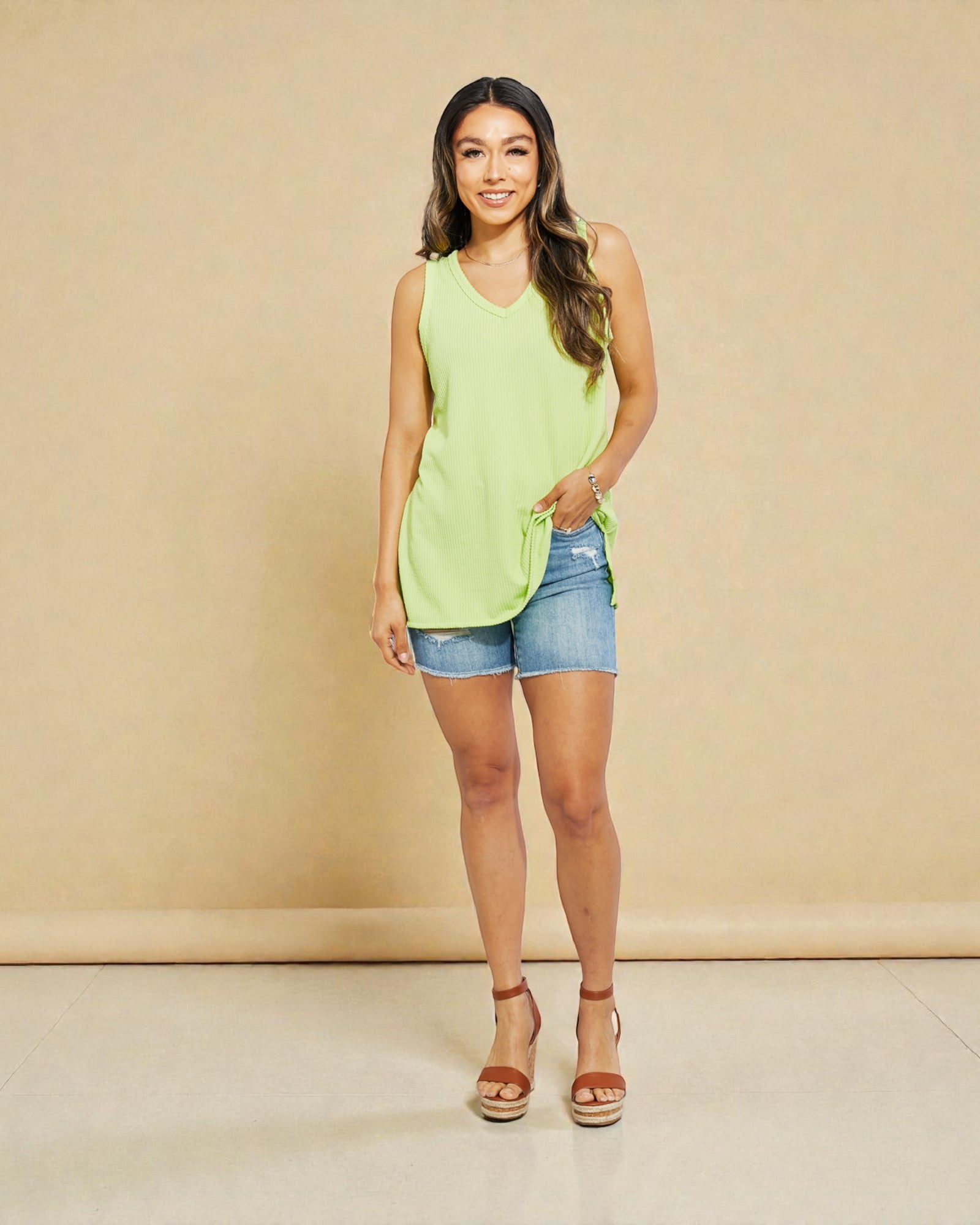 Woman wearing a light green sleeveless top and denim shorts against a beige background