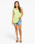 A woman modeling a sleeveless lime green V-neck top with side tie details, paired with denim shorts and brown wedge sandals, against a light gray studio background.