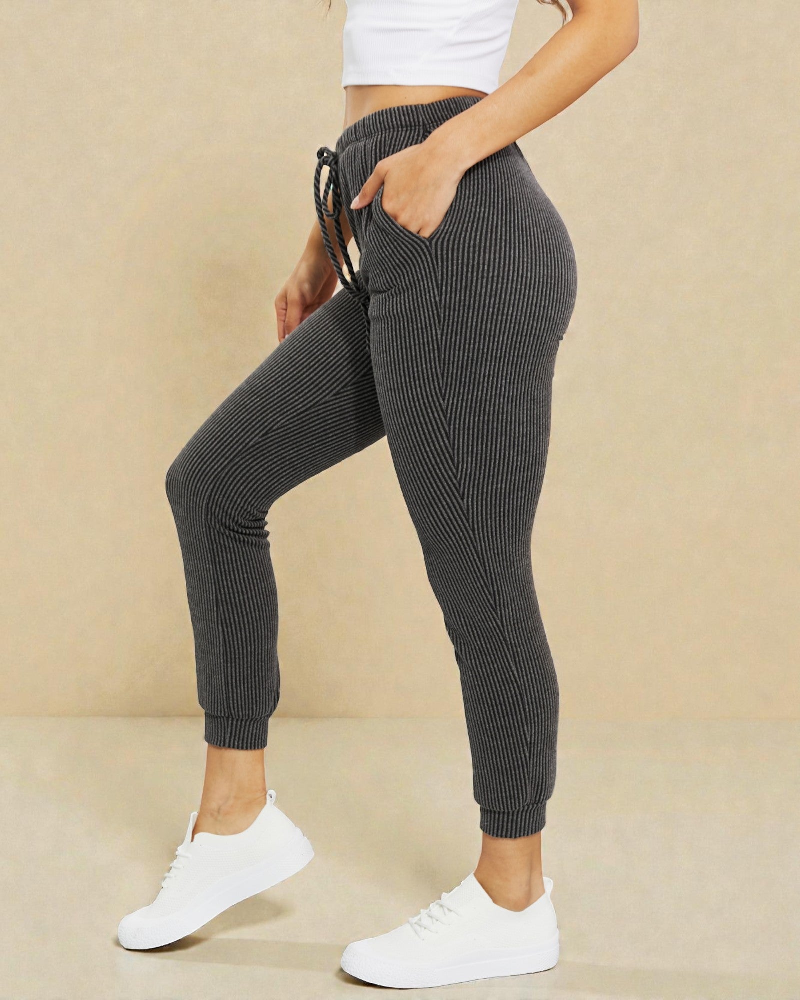 Person wearing dark ribbed jogger pants with a beige background