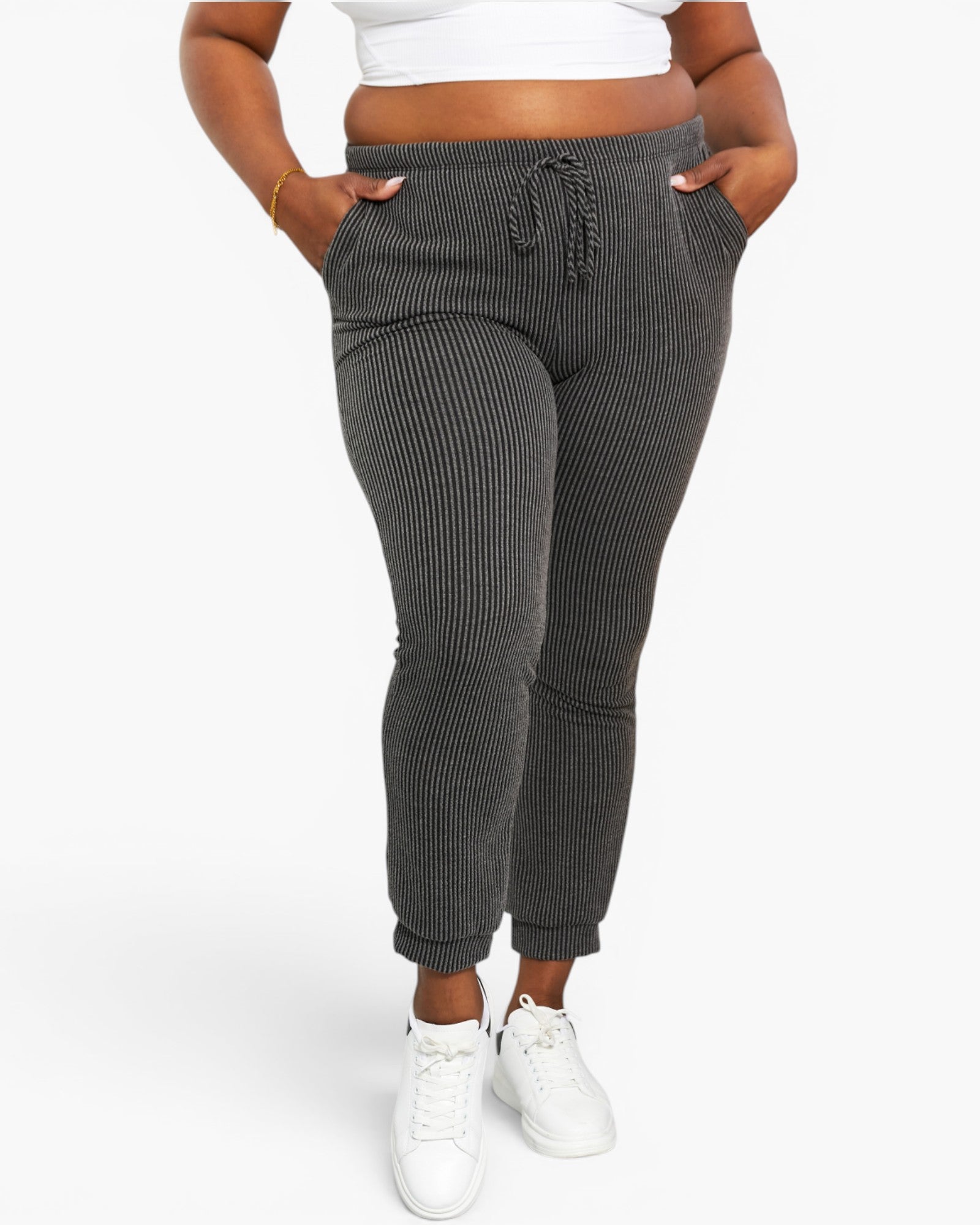 A person wearing dark gray ribbed jogger pants with a drawstring waistband, shown from the waist down against a light gray studio background.
