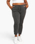 A person wearing dark gray ribbed jogger pants with a drawstring waistband, shown from the waist down against a light gray studio background.