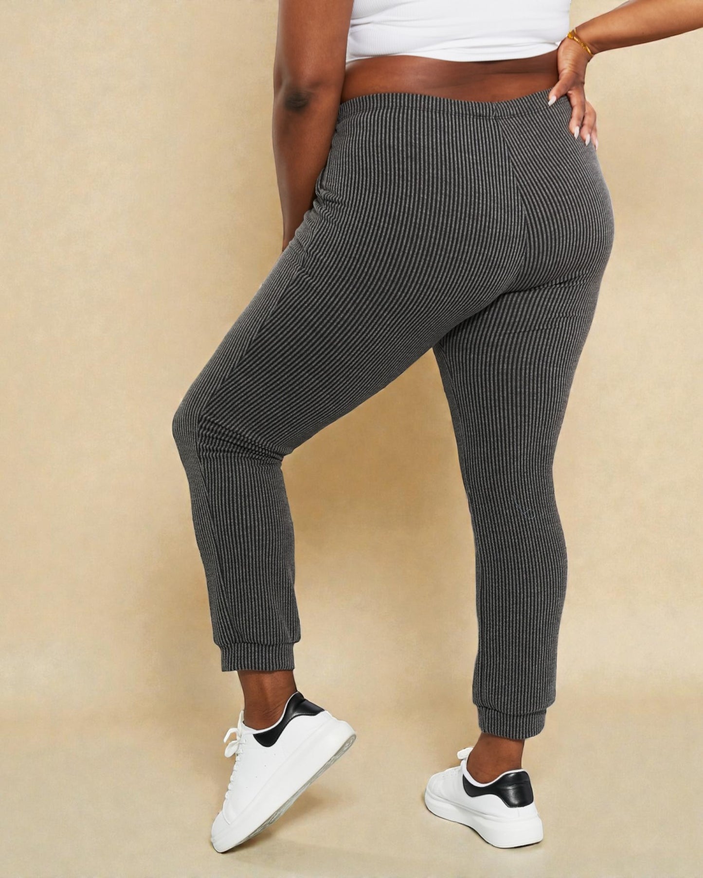 Person wearing gray ribbed jogger pants and white sneakers on a beige background
