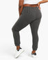A person wearing dark gray ribbed jogger pants with a white crop top and white sneakers, shown from the waist down against a light gray studio background.