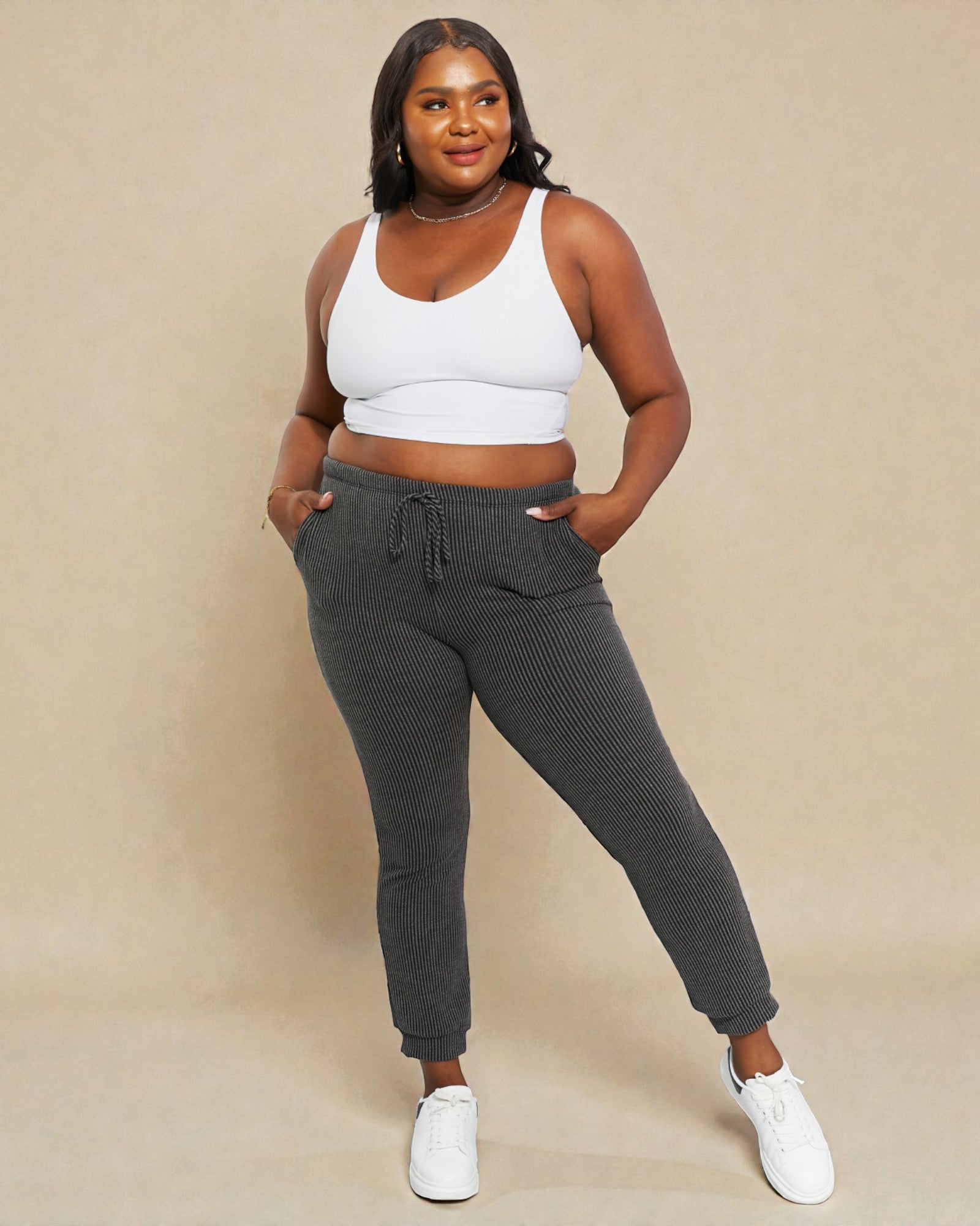 Woman wearing a white sports bra and gray sweatpants on a beige background