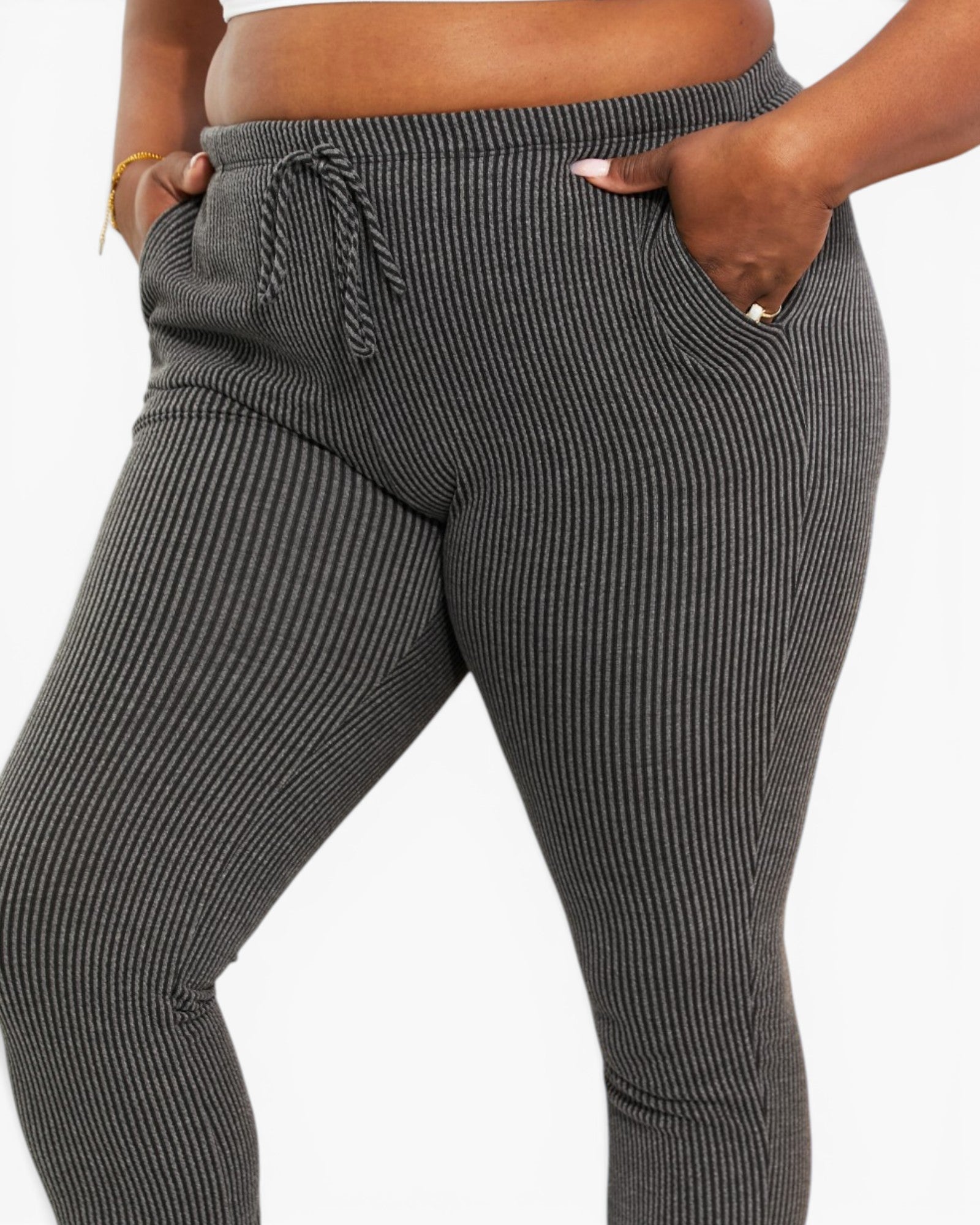 A close-up of a person wearing dark gray and black vertically striped ribbed lounge pants with side pockets and a drawstring waistband, shown against a plain light background.