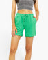 A model wearing bright green ribbed knit shorts with a matching drawstring waistband, paired with a gray ribbed crop top, against a plain white background.