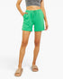 A model wearing bright green ribbed knit shorts with a drawstring waist, styled with a gray crop top and beige slide sandals against a plain white background.