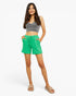 A woman modeling bright green drawstring shorts with a gray crop top and beige slide sandals, standing against a plain white studio background.