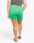 A person shown from the back wearing bright green ribbed shorts, a gray cropped top, and tan slide sandals against a plain light gray studio background.