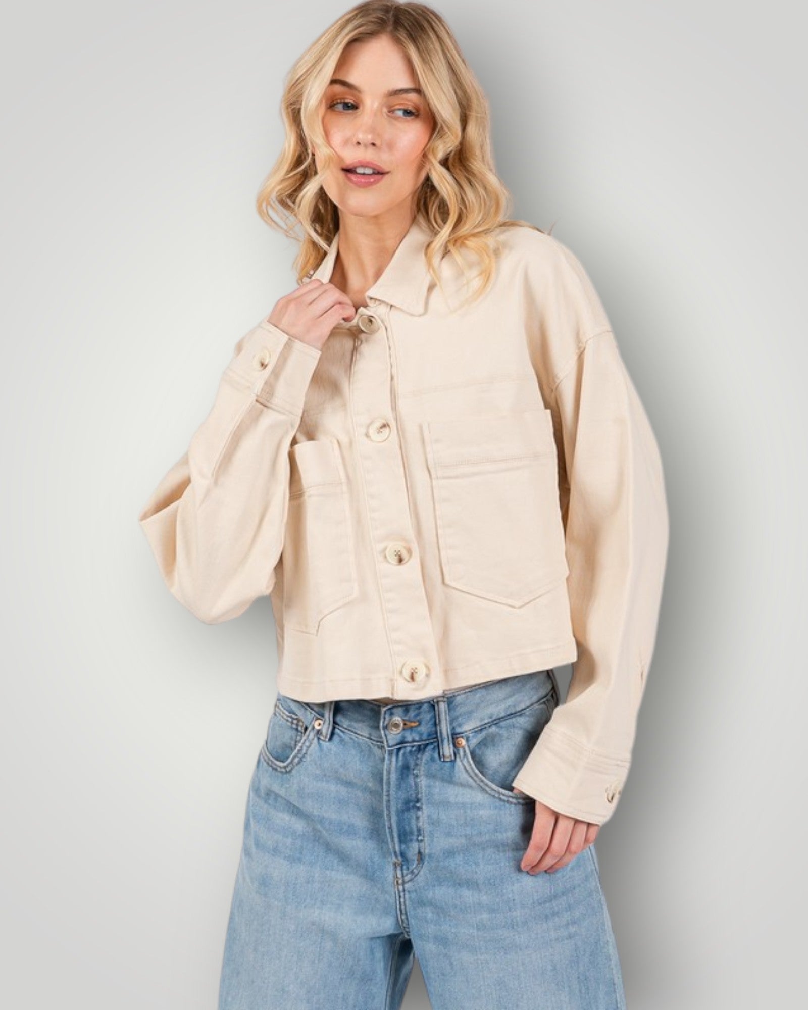 Woman wearing a beige jacket and blue jeans against a plain background