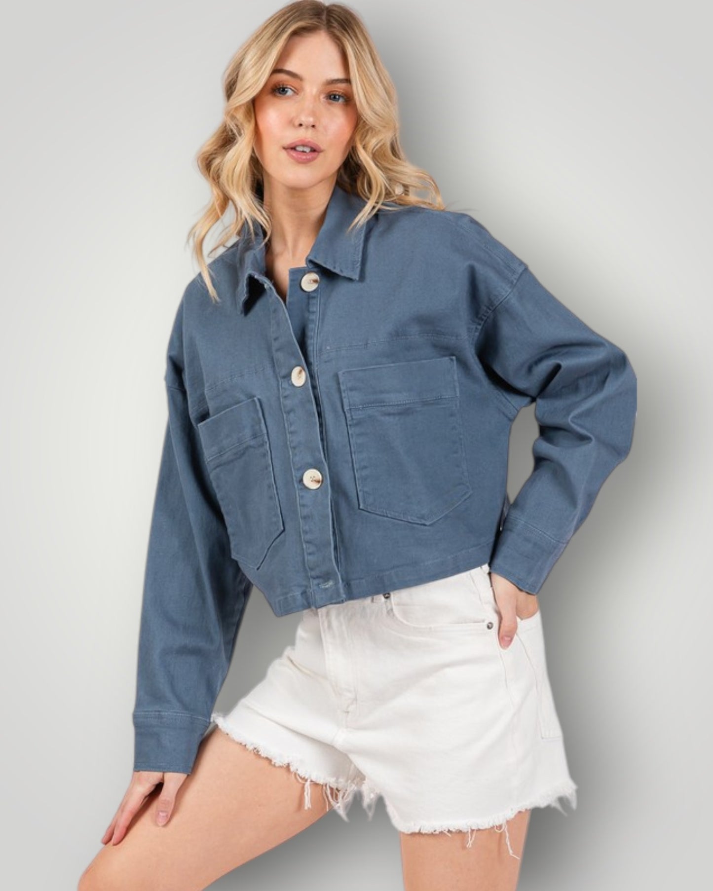 Woman wearing a blue denim jacket and white shorts on a plain background