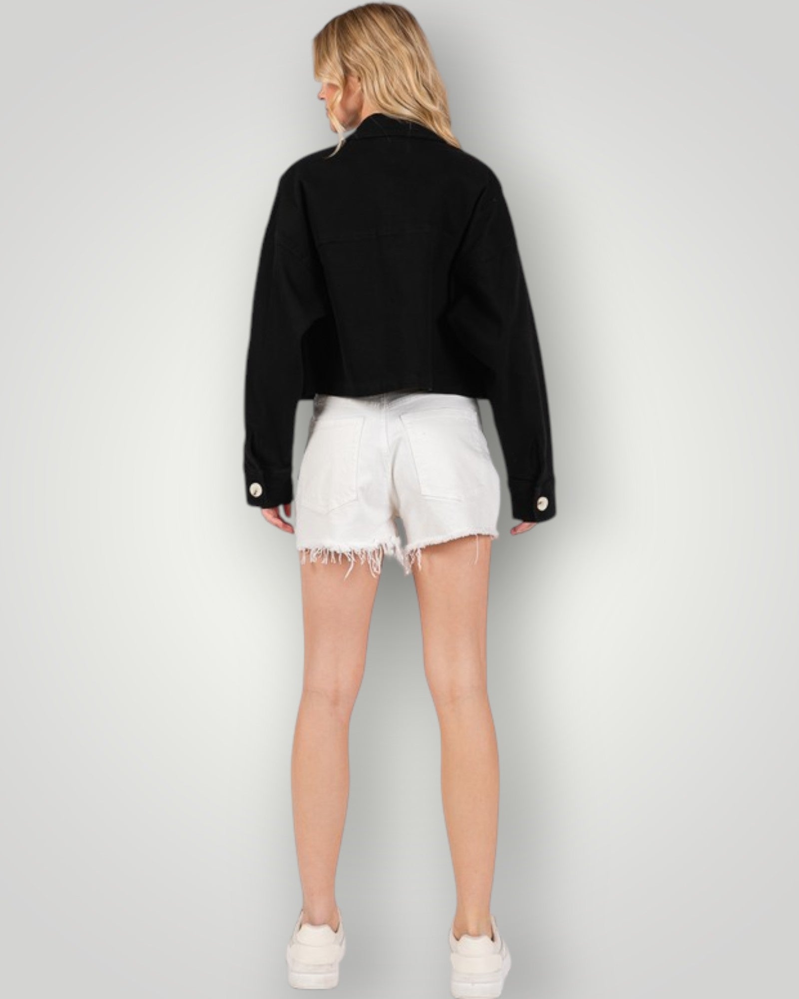 Person wearing a black jacket and white shorts on a plain background