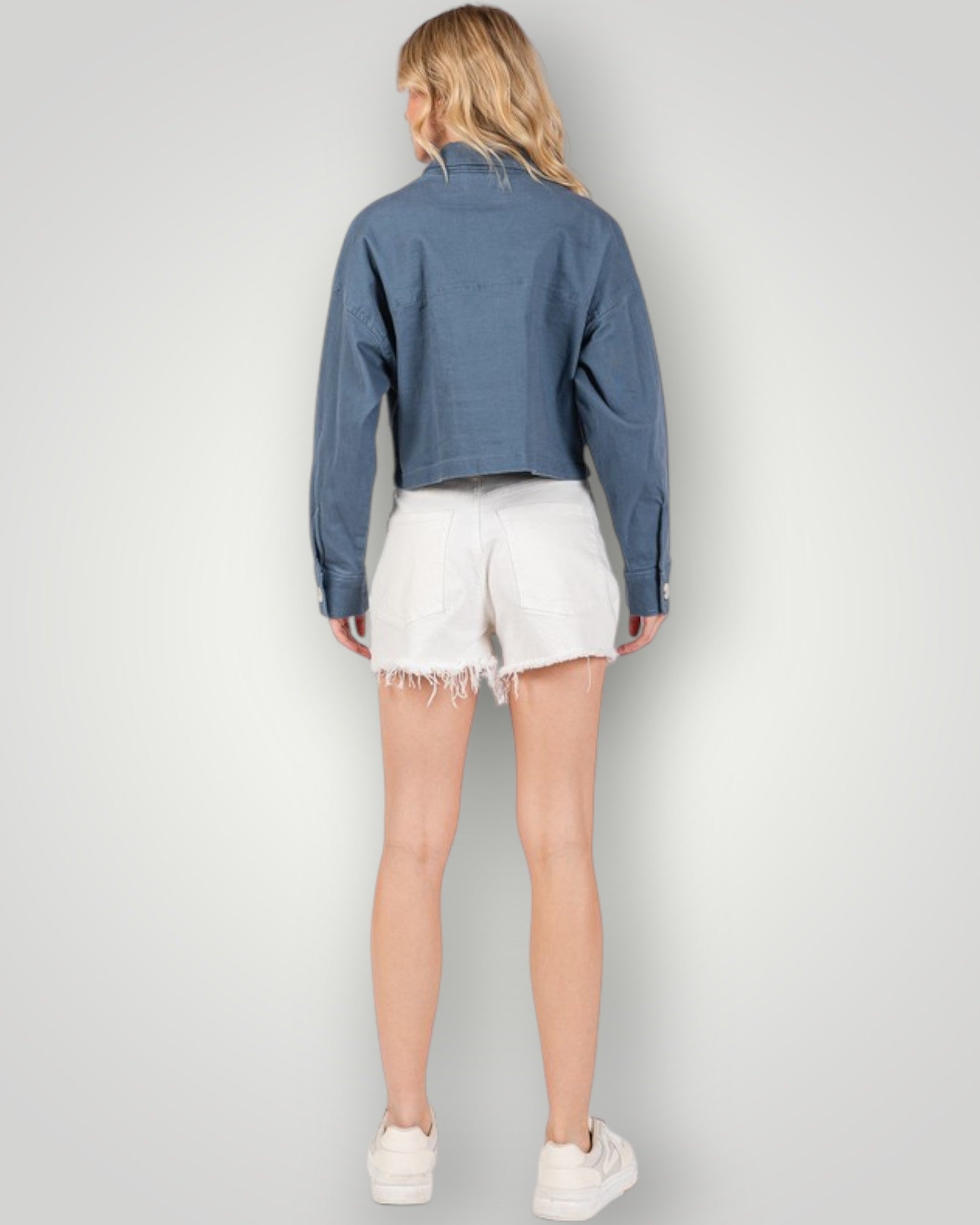 Person wearing a blue denim jacket and white shorts on a plain background
