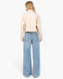 A woman shown from the back wearing a light beige cropped button-up shirt and light blue wide-leg jeans, photographed against a clean white studio background.