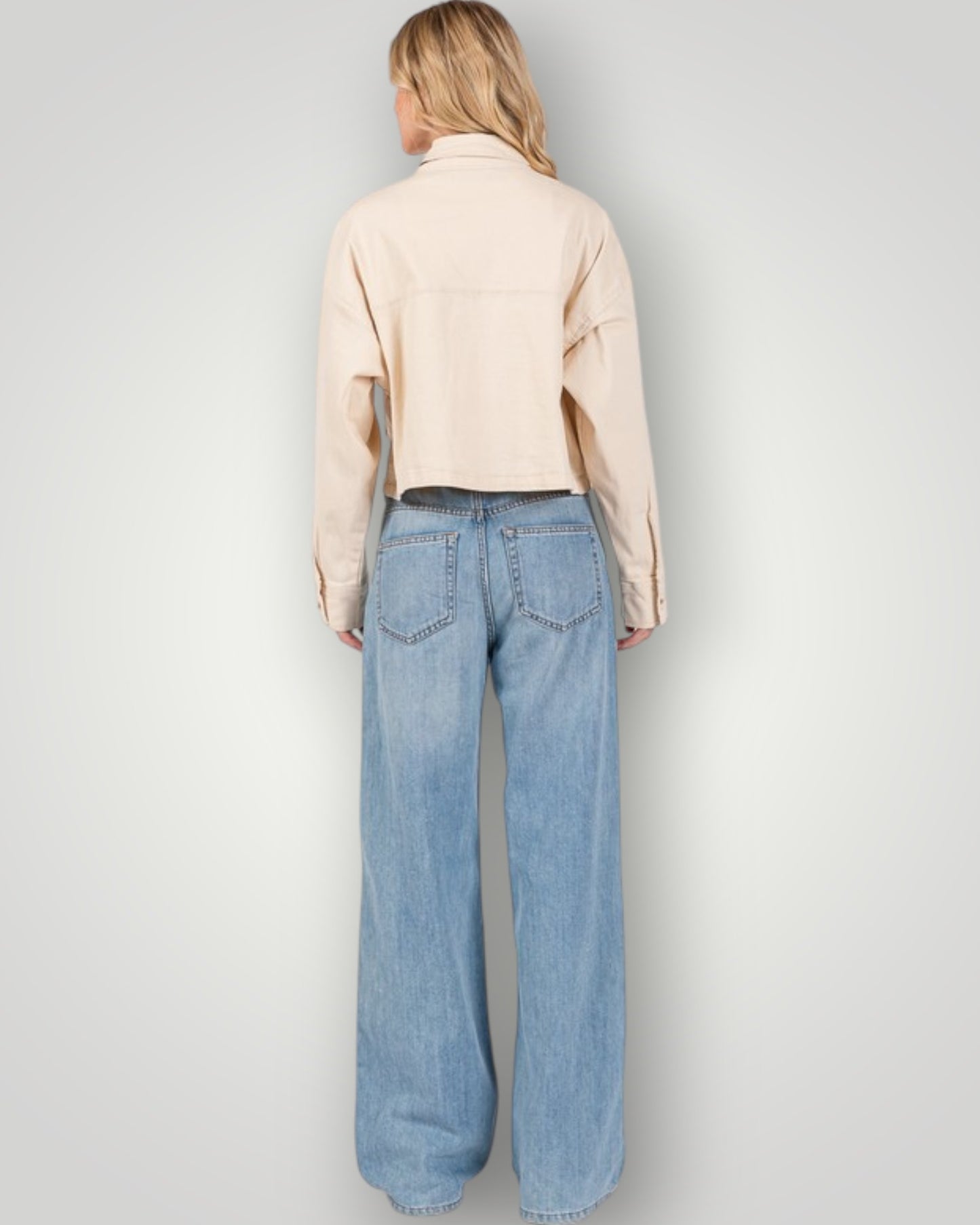 Person wearing a beige shirt and blue jeans on a plain background