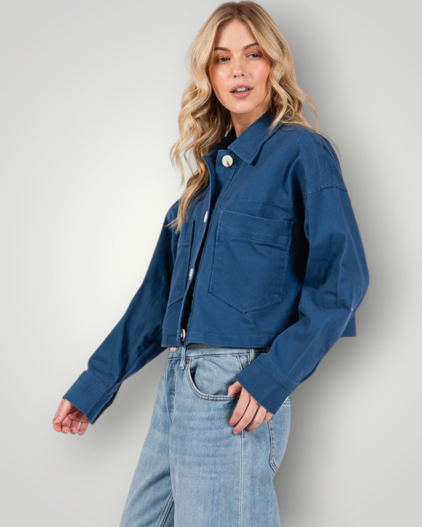 Woman wearing a blue jacket and jeans against a plain background