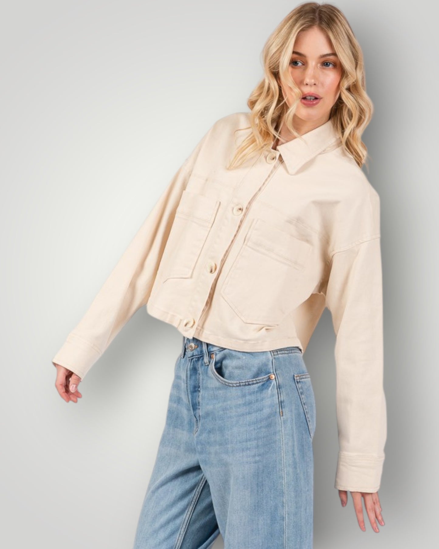 Woman wearing a beige jacket and blue jeans against a plain background