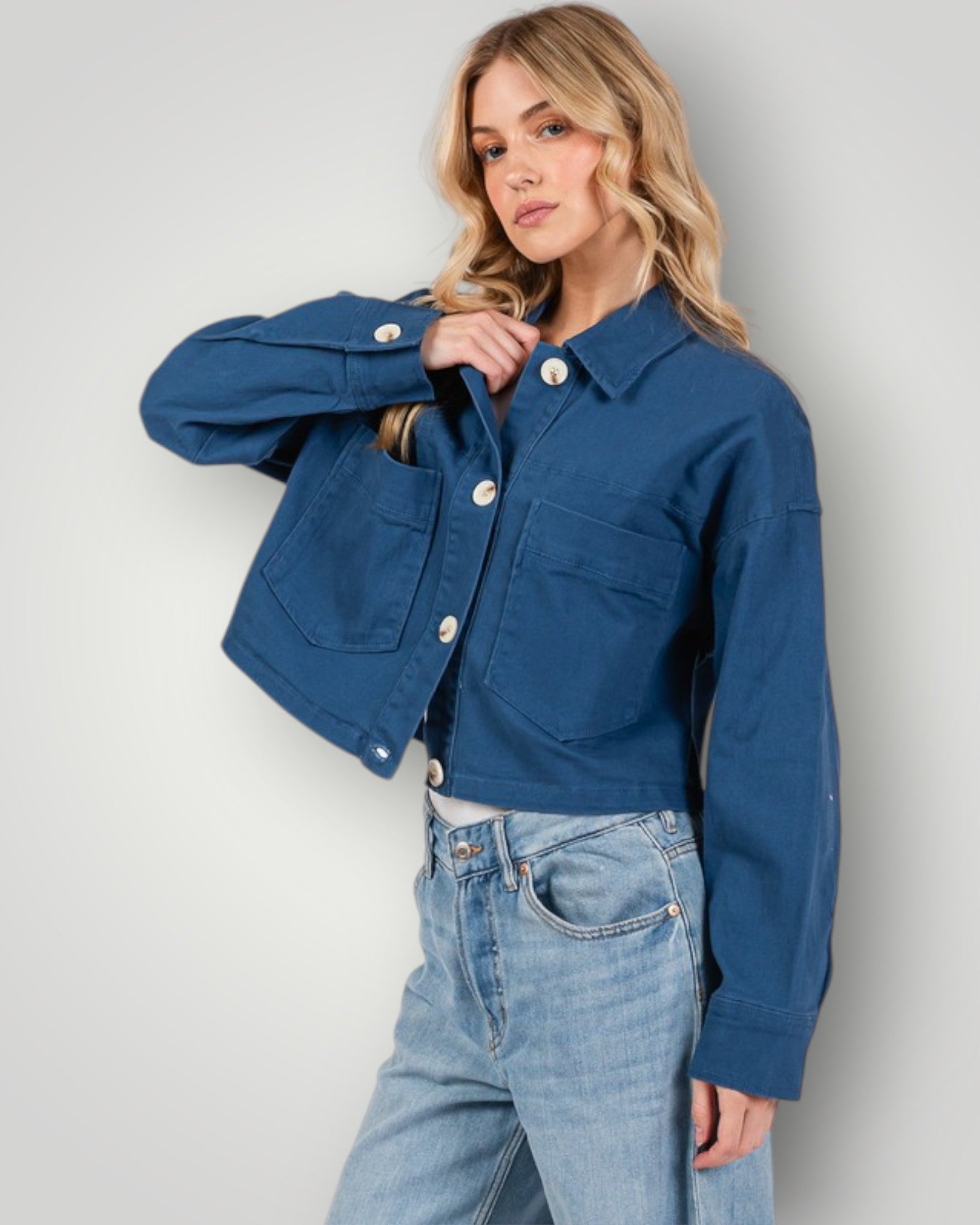 Woman wearing a blue denim jacket and jeans against a plain background