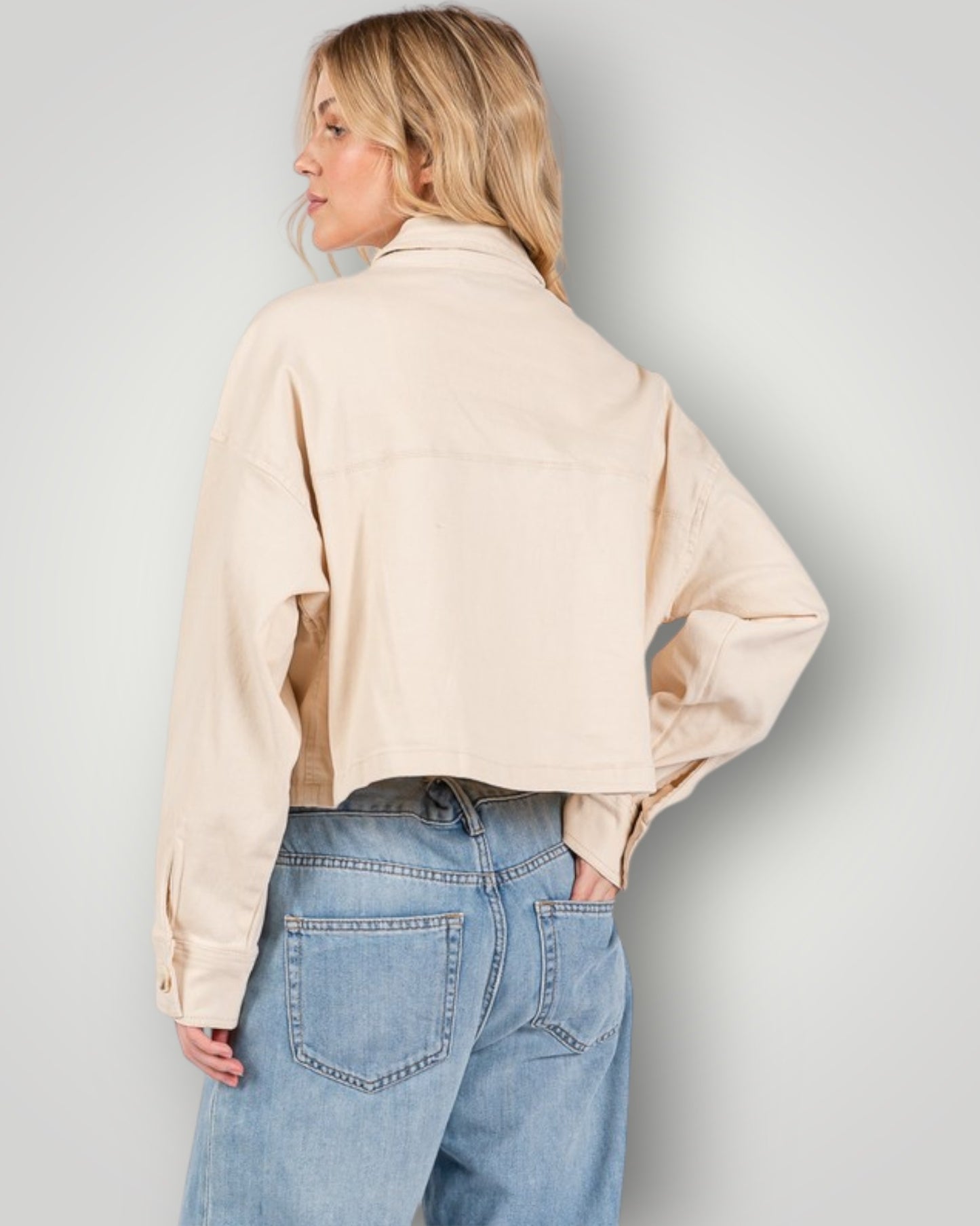 Person wearing a beige shirt and blue jeans against a plain background
