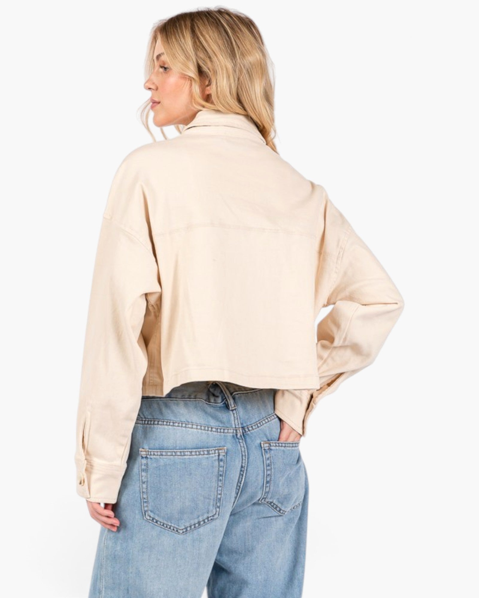 A woman shown from the back wearing a light beige cropped utility jacket and light blue jeans against a plain white background.