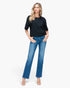 A woman modeling a black short-sleeve crewneck top and blue flare jeans against a plain white studio background.