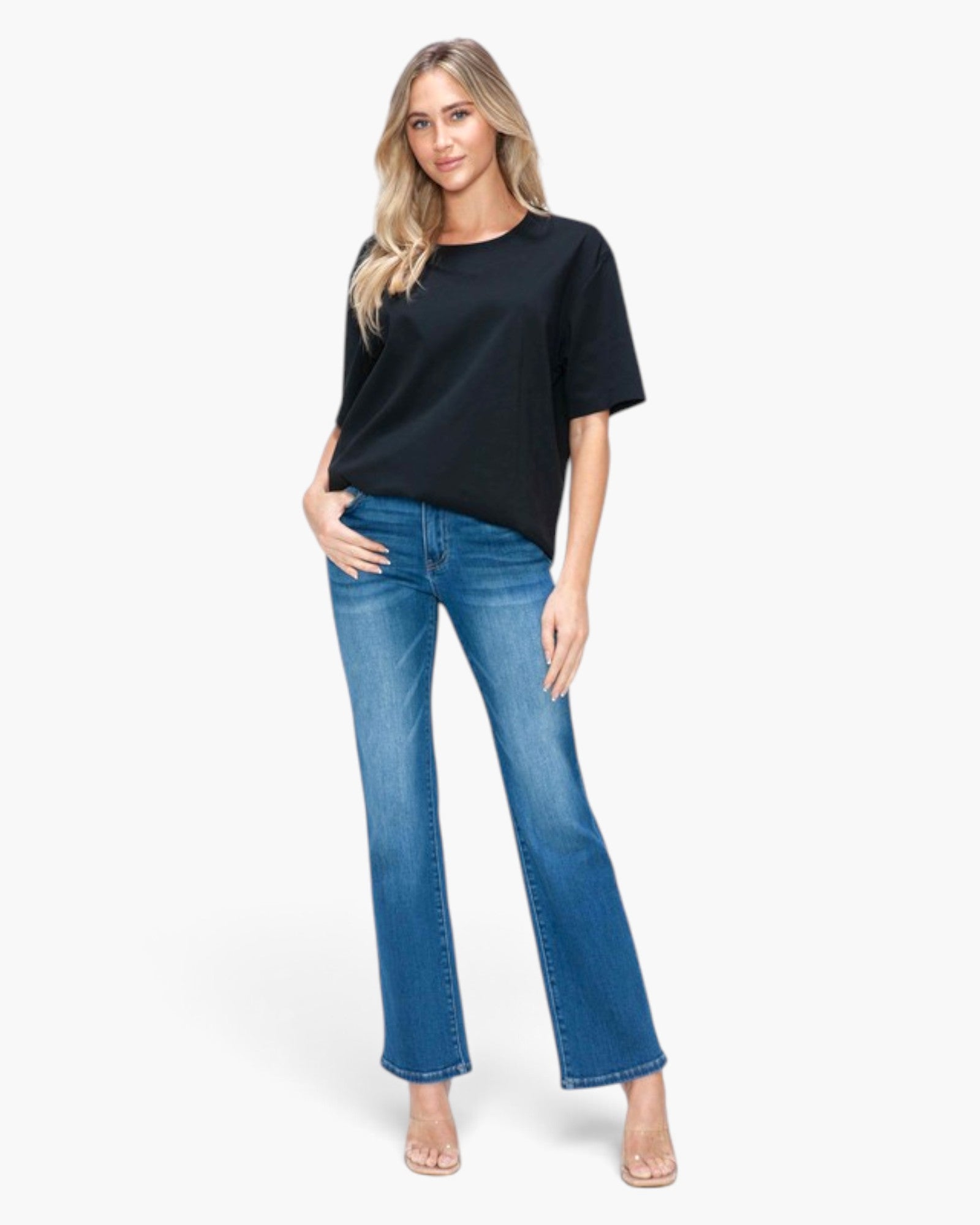 A woman modeling a black short-sleeve t-shirt and blue flare jeans against a plain white studio background.