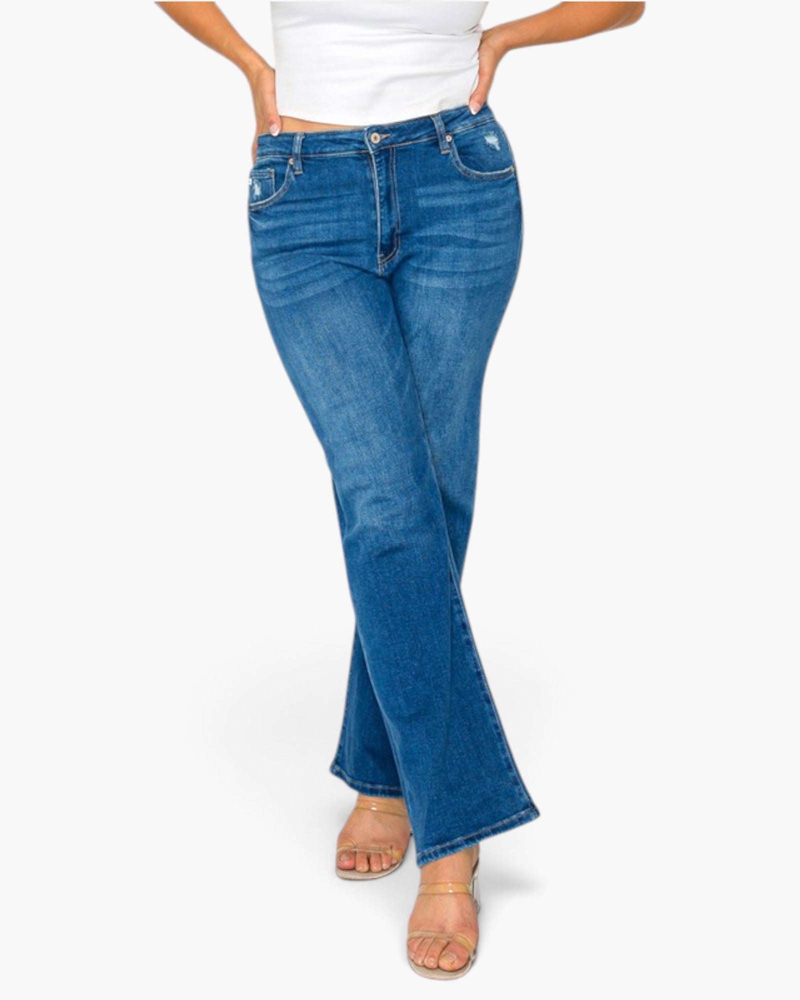 A model wearing a pair of medium-wash blue flare jeans with a white cropped top and beige sandals, shown from the waist down against a plain white background.