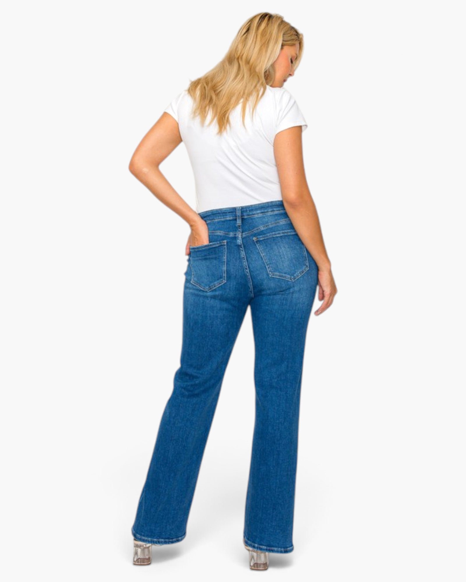 A woman shown from the back wearing blue flare jeans, a white t-shirt, and silver high heels against a plain white studio background.