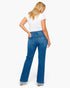 A woman shown from the back wearing blue flare jeans, a white t-shirt, and silver high heels against a plain white studio background.