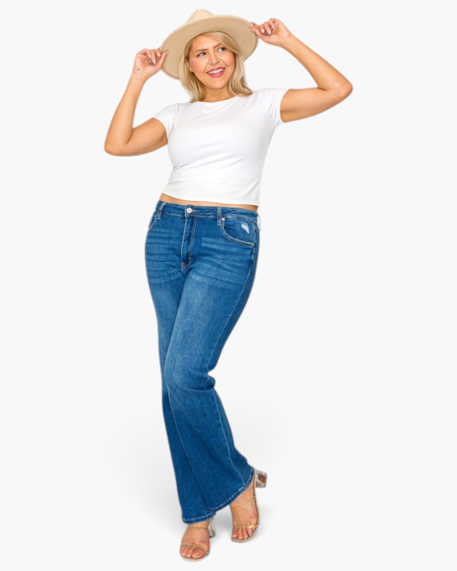 A woman modeling blue flare jeans, a white crop top, and a beige cowboy hat against a plain white background.