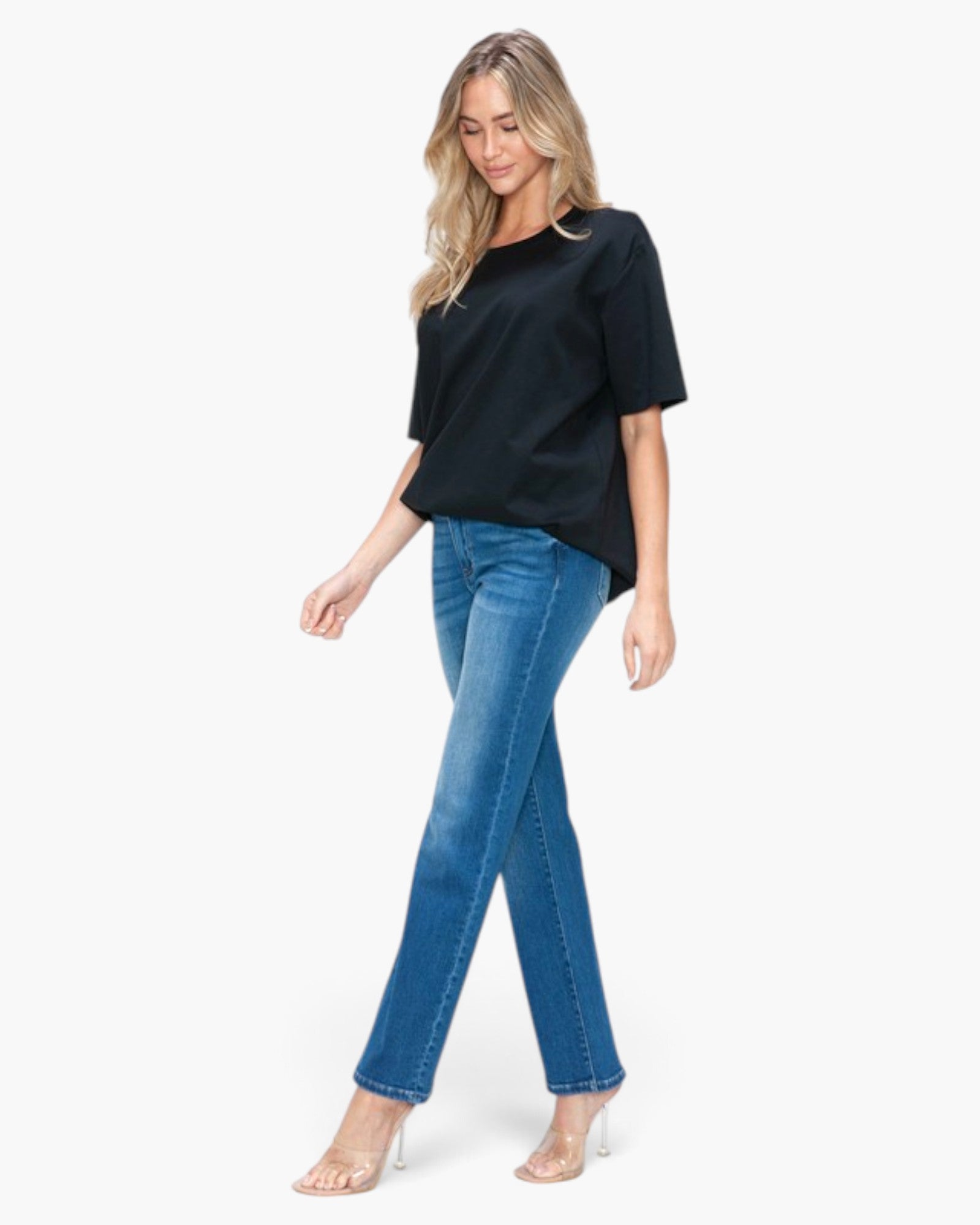 A woman modeling a black short-sleeve top and blue jeans against a plain white background.