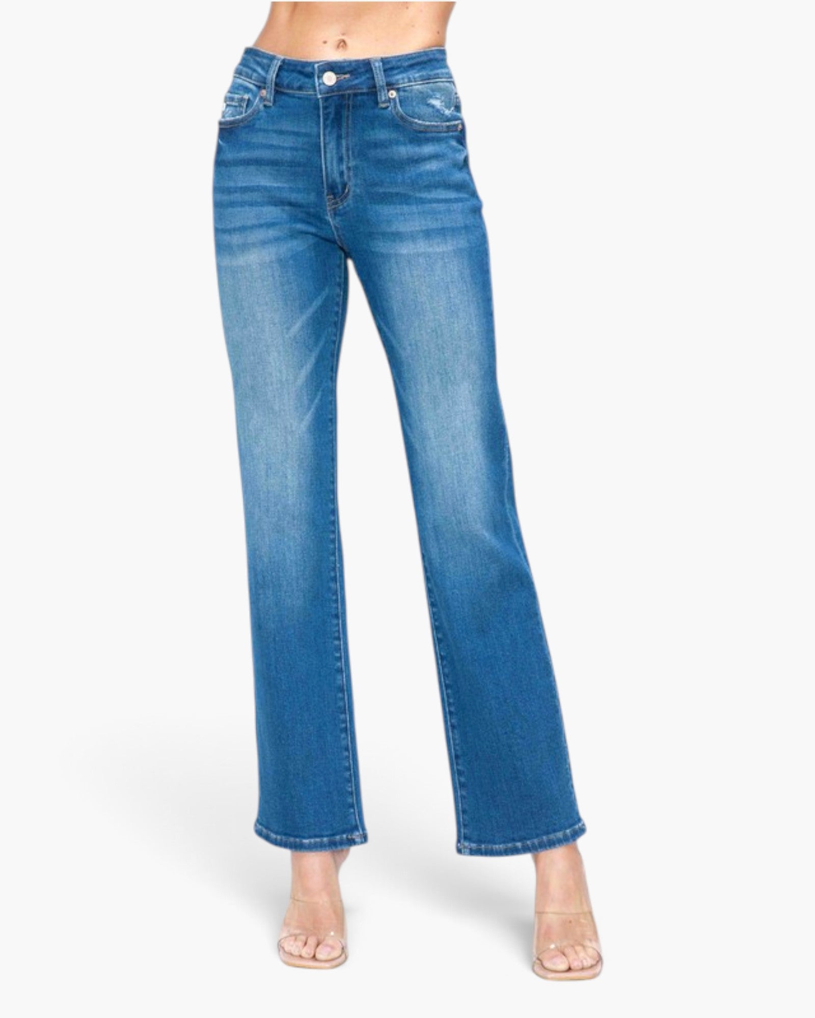 A model wearing a pair of medium-wash blue denim jeans with a straight-to-flare leg, styled with clear high-heeled sandals against a plain white background.