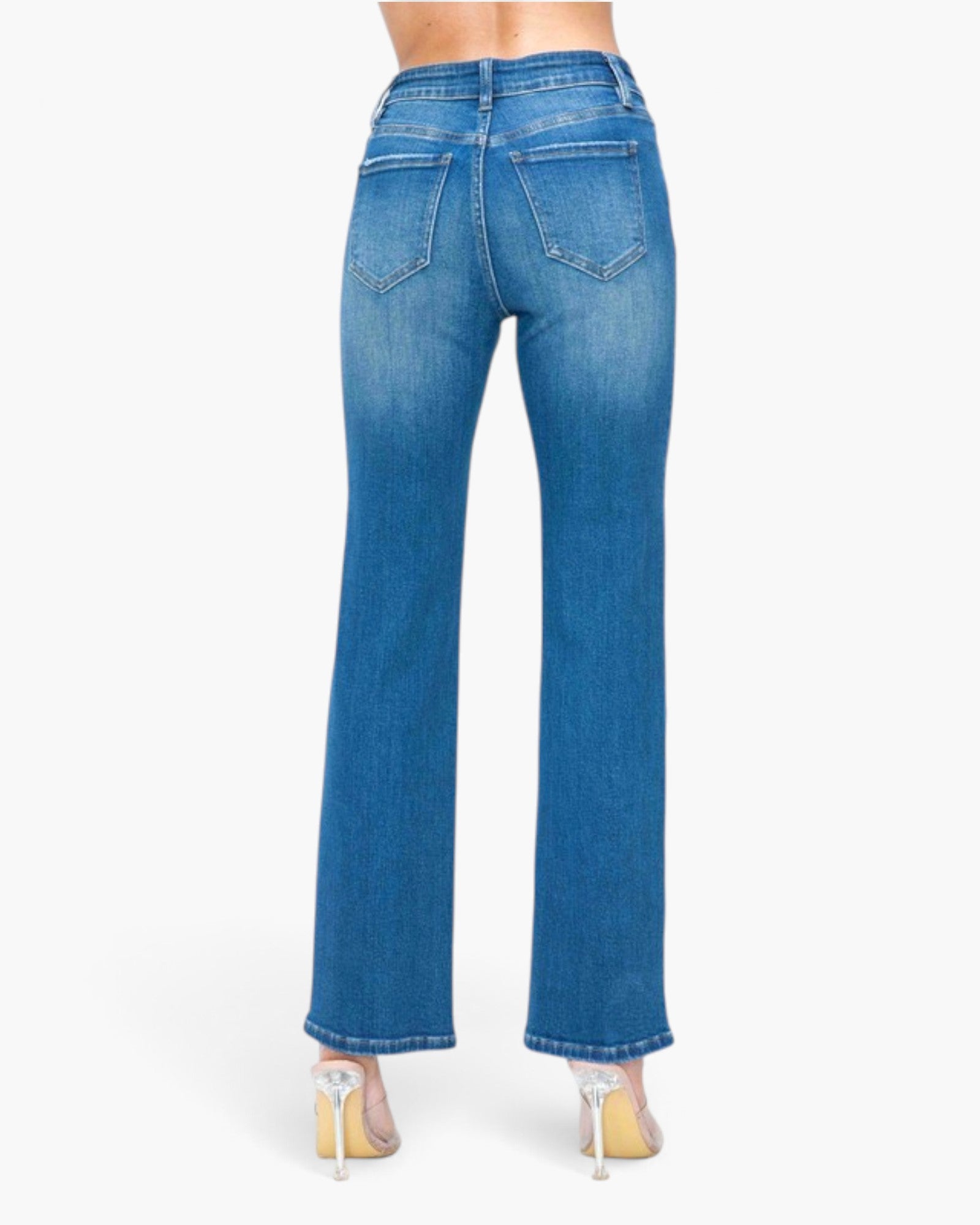 Rear view of a model wearing medium wash blue denim flare jeans with a high waist and straight-to-flared leg, paired with clear high-heeled shoes against a plain white background.