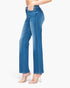 A model wearing a pair of medium wash blue denim jeans with a straight-to-wide leg fit, paired with clear high-heeled sandals, shown from the waist down against a plain white background.