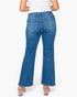 Rear view of a person wearing blue flare jeans with a white top and clear high-heeled sandals against a light gray studio background.