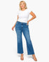 A woman modeling a pair of medium-wash blue flare jeans with a white t-shirt and clear high-heeled sandals, standing against a solid white background.