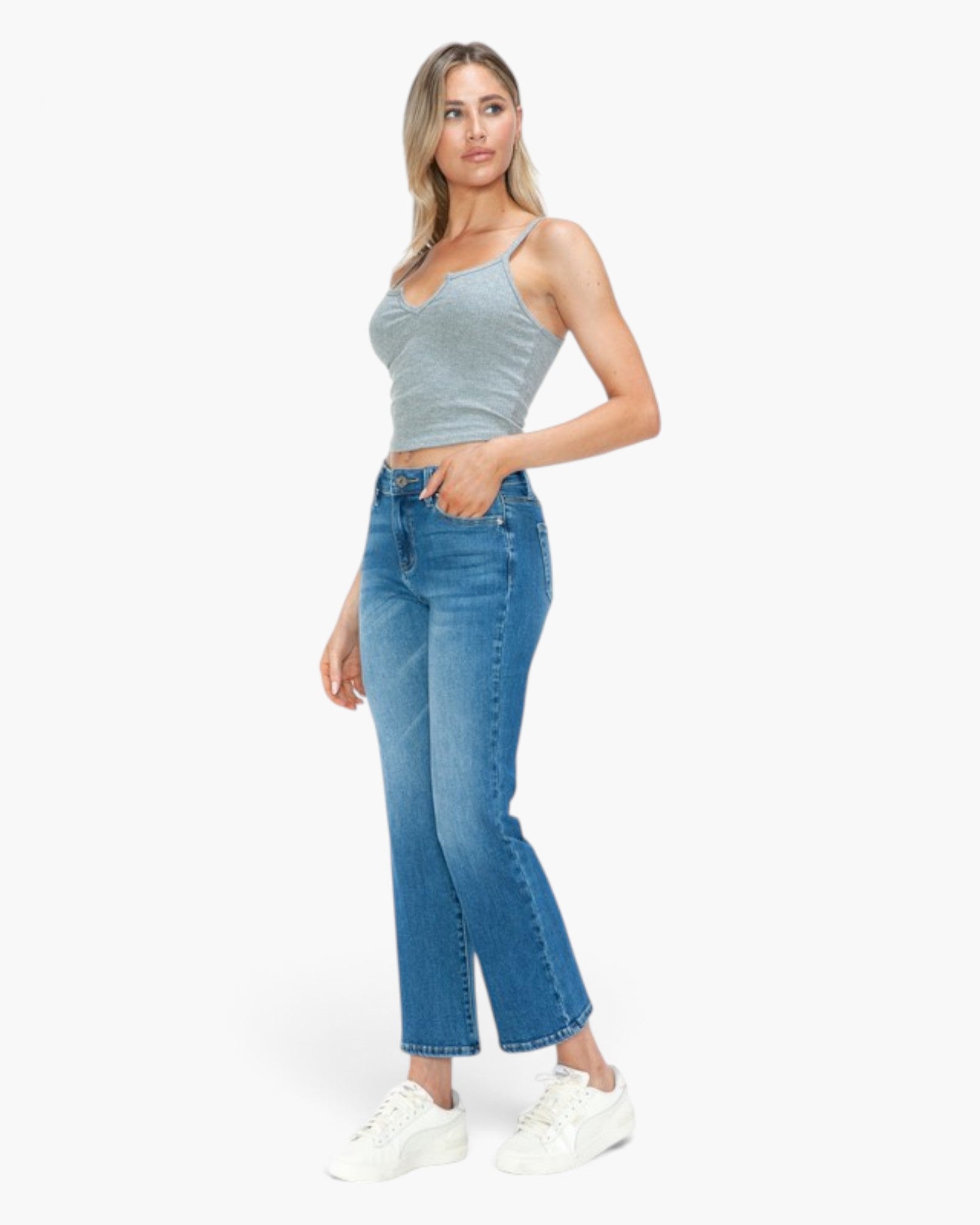 A woman modeling a light gray ribbed camisole top and blue cropped flare jeans with white sneakers, standing against a plain white studio background.